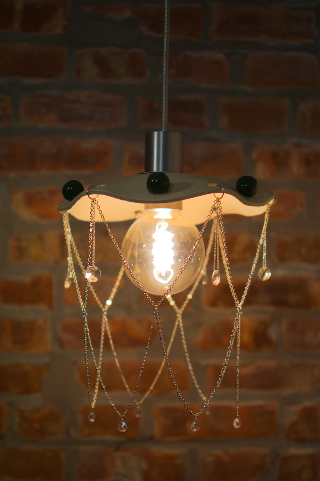 Decorative pendant light with hanging chandelier crystals against a brick wall.