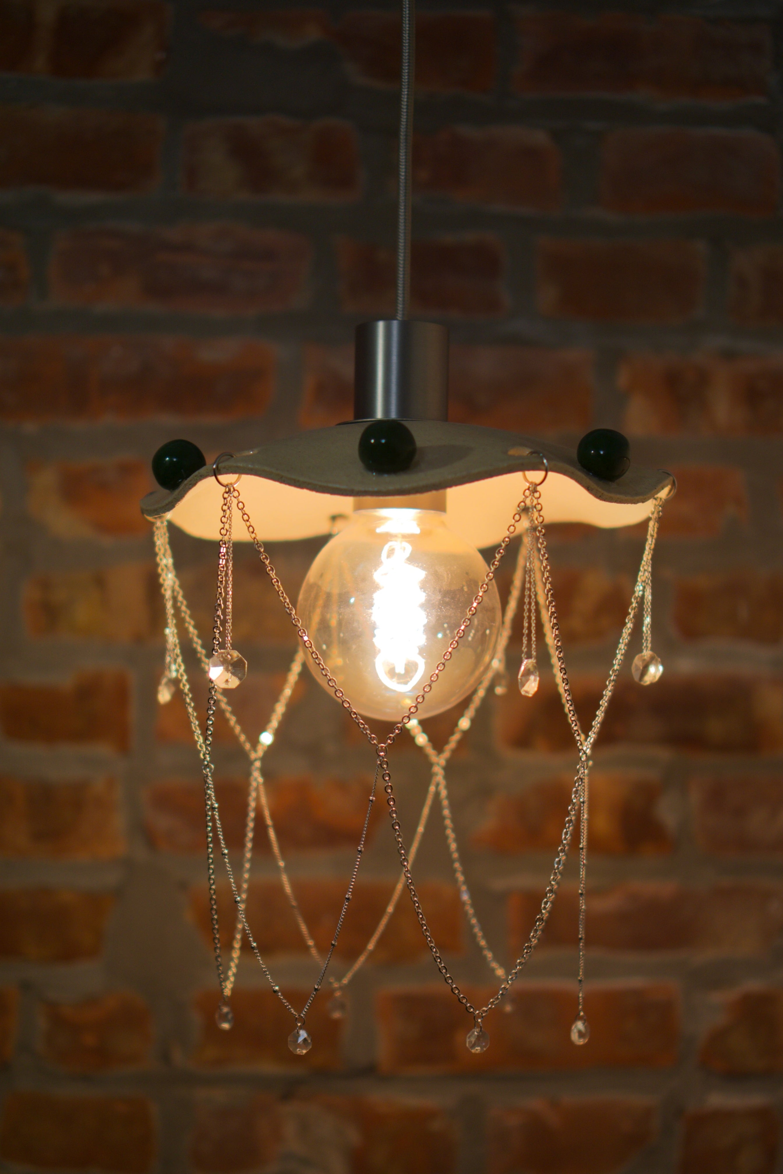 Decorative pendant light with hanging chandelier crystals against a brick wall.